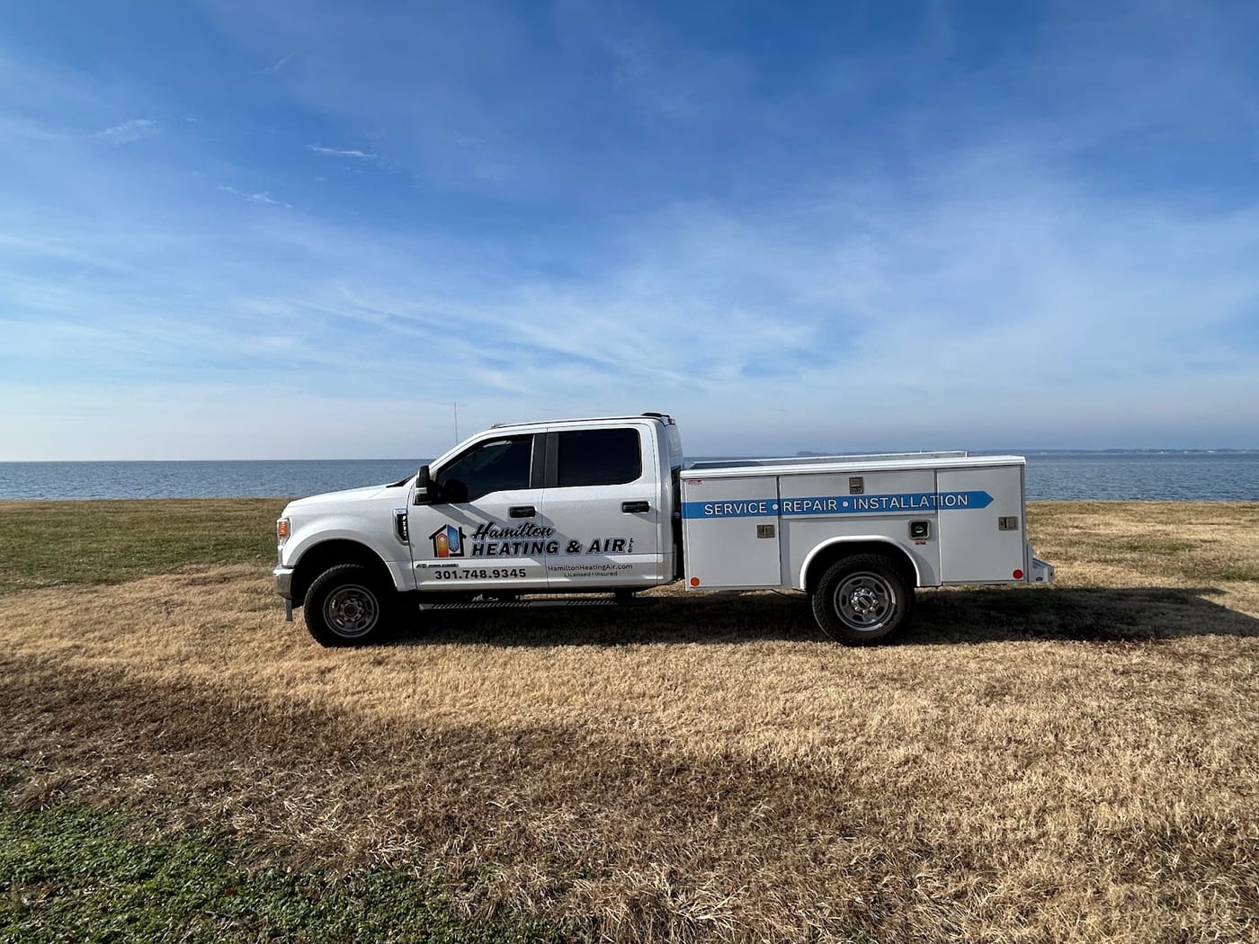 Hamilton Heating & Air service truck on the shoreline grass under a wide blue sky