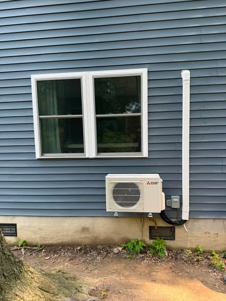 Ductless outdoor unit mounted low on blue siding under a window