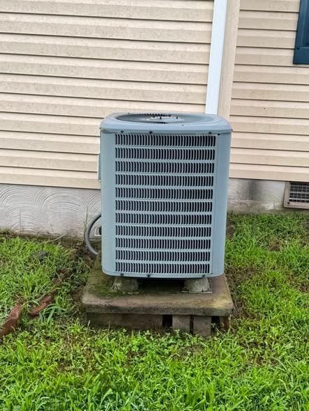 Outdoor condenser on a pad beside tan siding and a green lawn