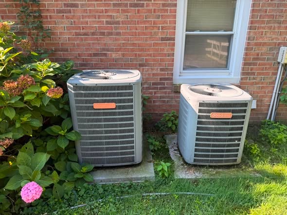 Two outdoor condensers beside a brick home with hydrangeas