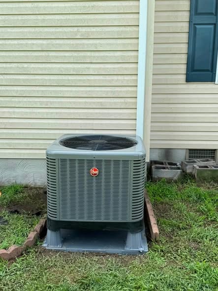New outdoor condenser on a pad beside tan siding