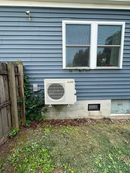 Ductless outdoor unit on blue siding beside a wood fence